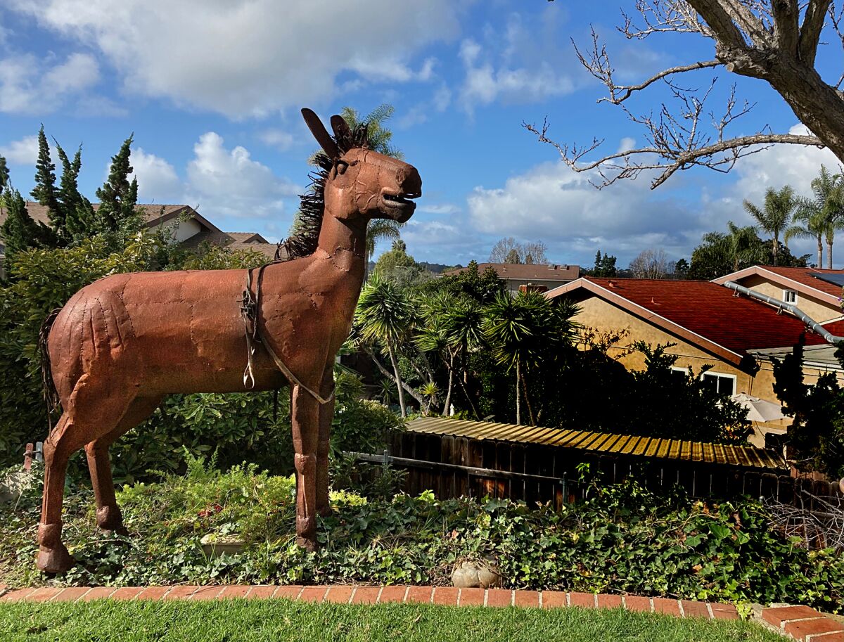 A metal sculpture of a mule by Ricardo Breceda stands amid avocado, persimmon and tangerine trees in a home's garden.