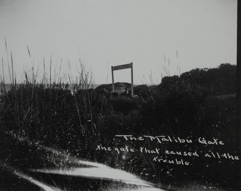 View of a man in a wagon, passing under a gate with a sign that reads "Malibu Rancho - Trespassers Strictly Prohibited." The land (present day Malibu, California) at this time was owned by Frederick and May Knight Rindge.