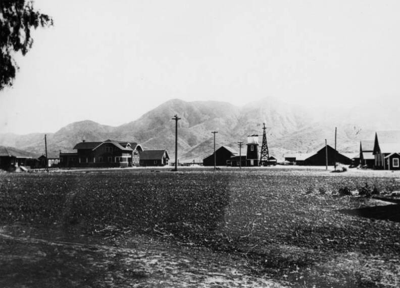 An oil rig can be seen mid-photo, next to a tower-like structure, possibly a silo. The mountains can be seen in the background. 