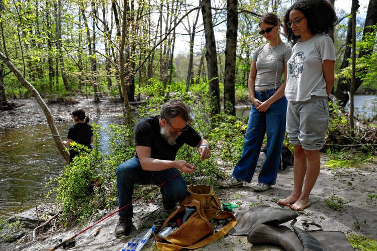 Northampton High School teacher Bob Melnik prepares a fishing line for students Annika Bergstreiser and Abigail Rivera while Ivy Lovejoy fishes along the Mill River as part of a homesteading class.